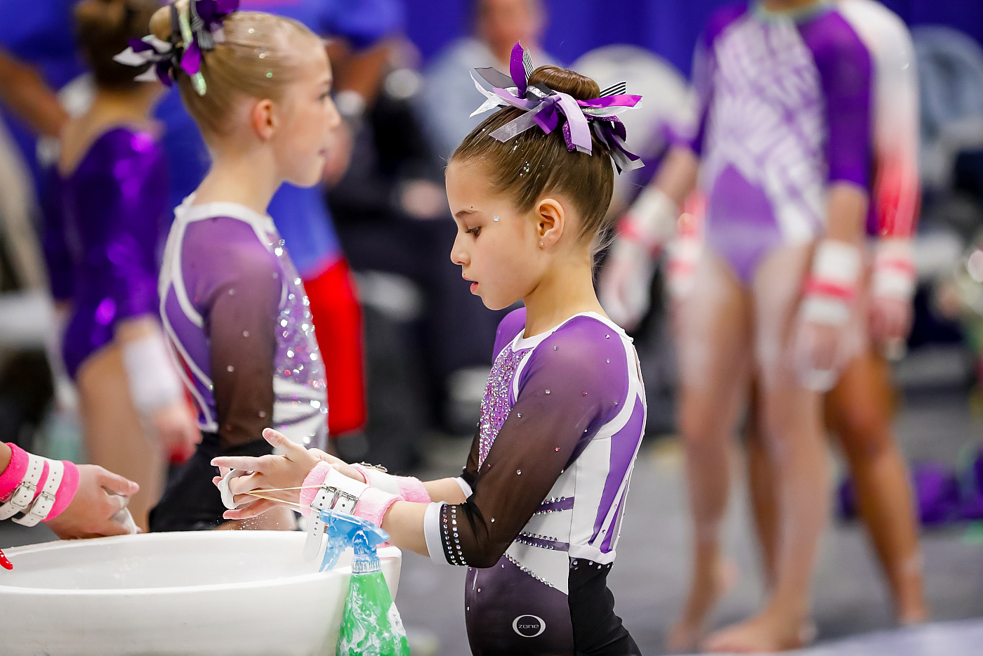 girl gymnast in purple leotard puts chalk on hands during gymnastics competition 