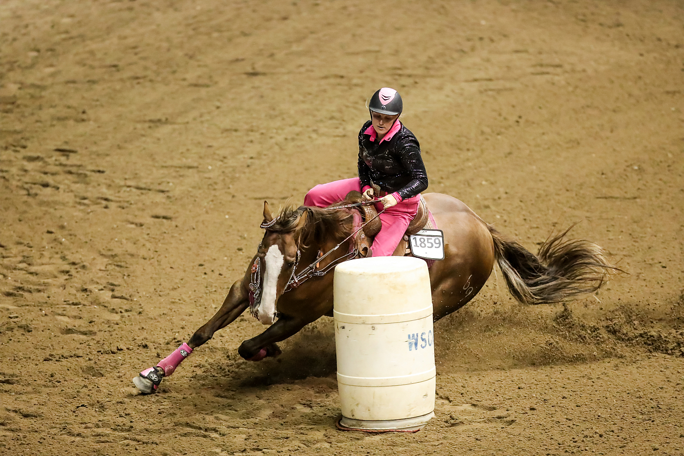 woman riding around barrel during equestrian competition pink pants, brown horse